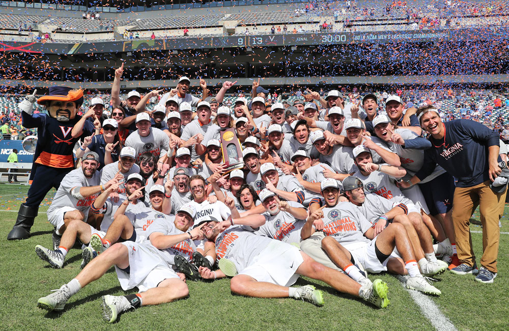 Men’s lacrosse team posing with the championship trophy as confetti falls