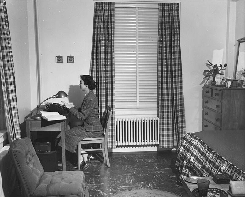 A female student types on a typewriter in a dorm room