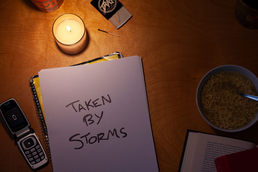 Taken by Storms written on a pad of paper, lit by candlelight as if the power is out